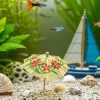 A small aquarium landscape consisting of a snail, a small sailboat and a miniature umbrella on the gravel.