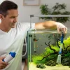 Man is using a gravel cleaner to clean his aquairum.