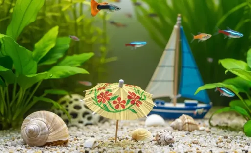 A small aquarium landscape consisting of a snail, a small sailboat and a miniature umbrella on the gravel.